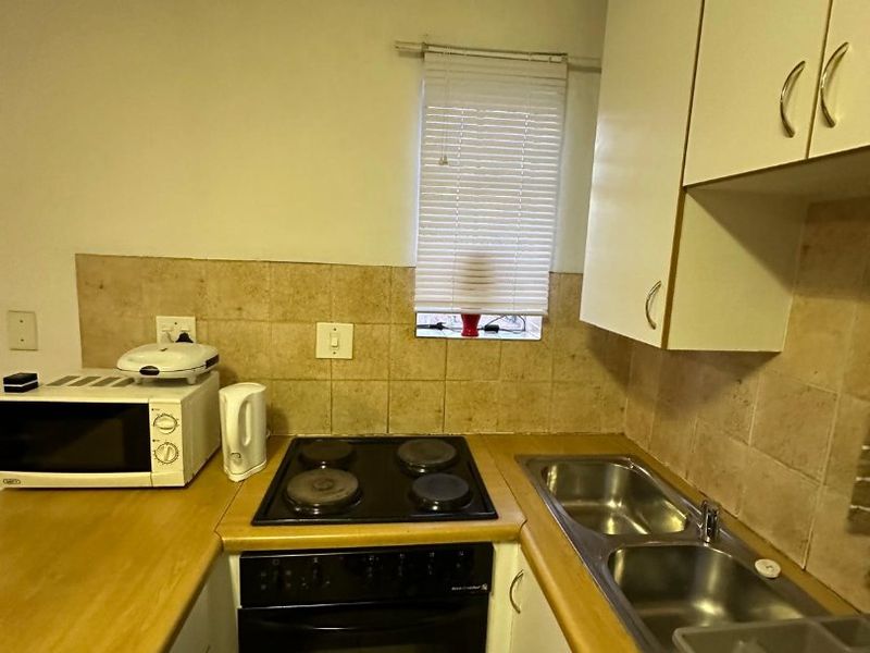 Compact kitchen featuring built-in cabinetry, laminate countertops, an electric hob and oven, and a double stainless steel sink with tiled backsplash.
