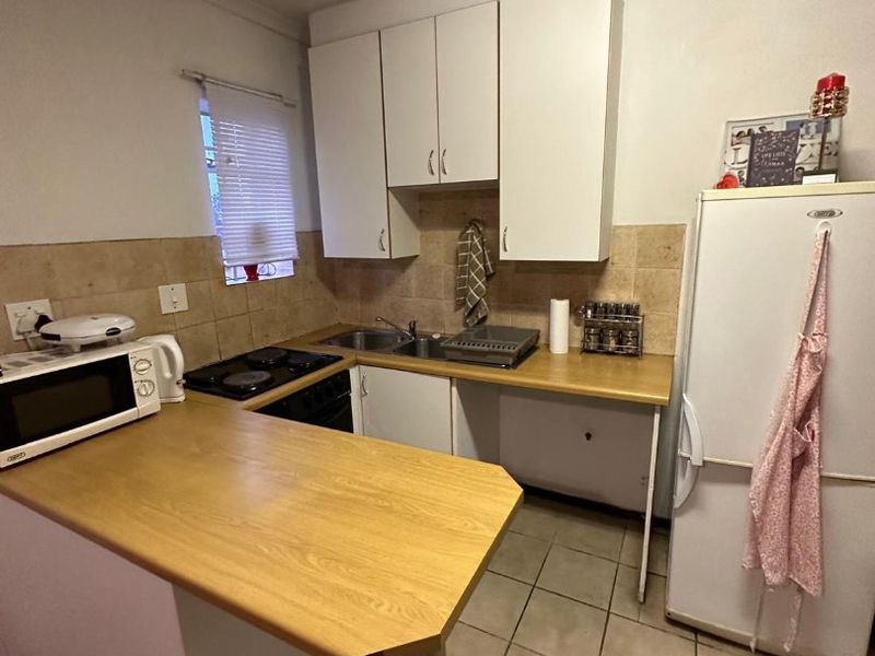 Compact kitchen featuring laminate countertops, tiled backsplash, tiled flooring, and functional built-in cabinetry with an integrated electric hob.
