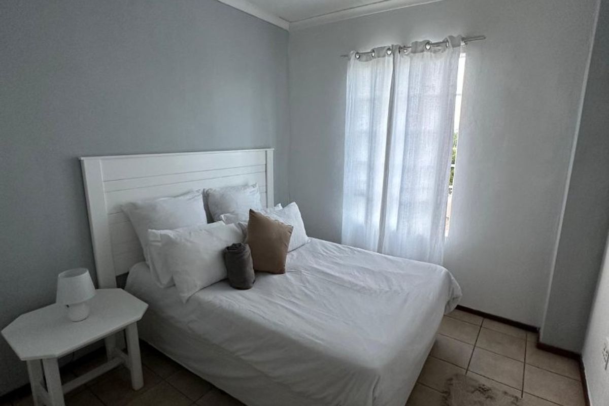 A functional bedroom featuring tiled flooring, neutral wall paint, and a window with installed curtain rod, providing a clean and simple living space.