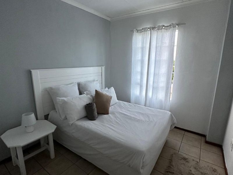 A functional bedroom featuring tiled flooring, neutral wall paint, and a window with installed curtain rod, providing a clean and simple living space.