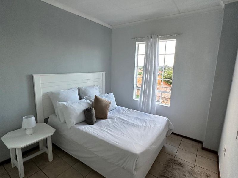 A functional bedroom featuring tiled flooring, a ceiling-mounted spotlight fixture, and a window with security bars, offering a simple and clean living space.