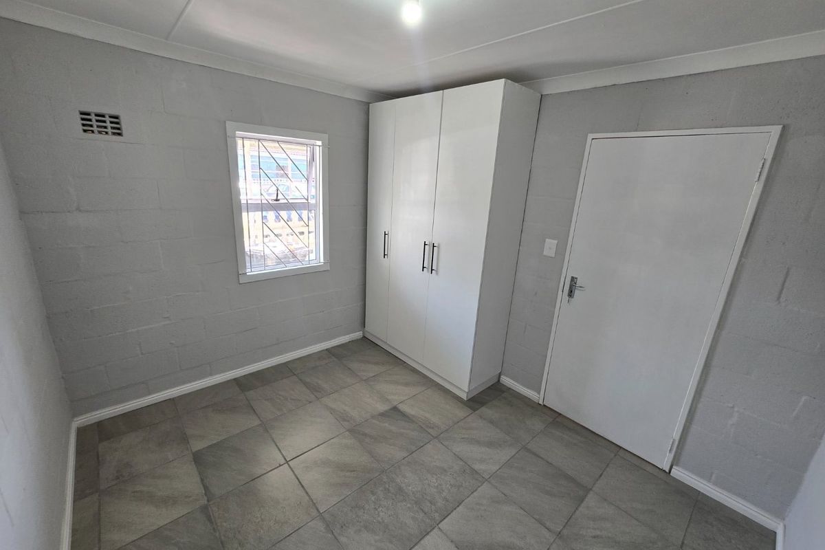 A clean, empty bedroom featuring grey tiled flooring, exposed blockwork walls, and a modern white built-in wardrobe.