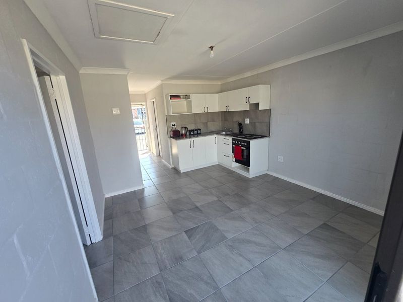 Open-plan living area featuring a compact kitchen with white cabinetry, tiled flooring, and integrated cooking appliances.