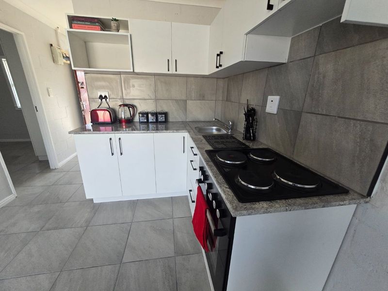 Compact kitchen featuring white cabinetry, granite countertops, a built-in electric oven and hob, and neutral tiled finishes.
