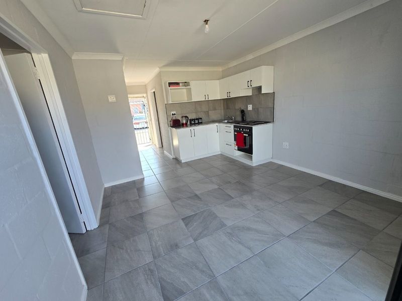 Open-plan kitchen and living area featuring modern grey floor tiles, white cabinetry, and built-in cooking appliances.