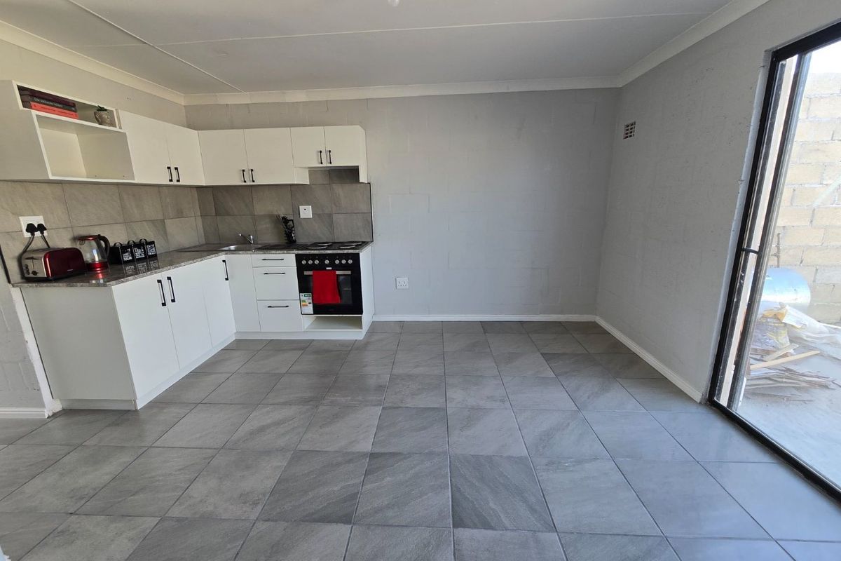 Modern open-plan kitchen featuring white cabinetry, grey tiled flooring, built-in oven and hob, and direct access to an outdoor area via sliding glass doors.