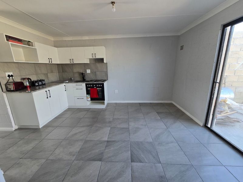Modern open-plan kitchen featuring white cabinetry, grey tiled flooring, built-in oven and hob, and direct access to an outdoor area via sliding glass doors.