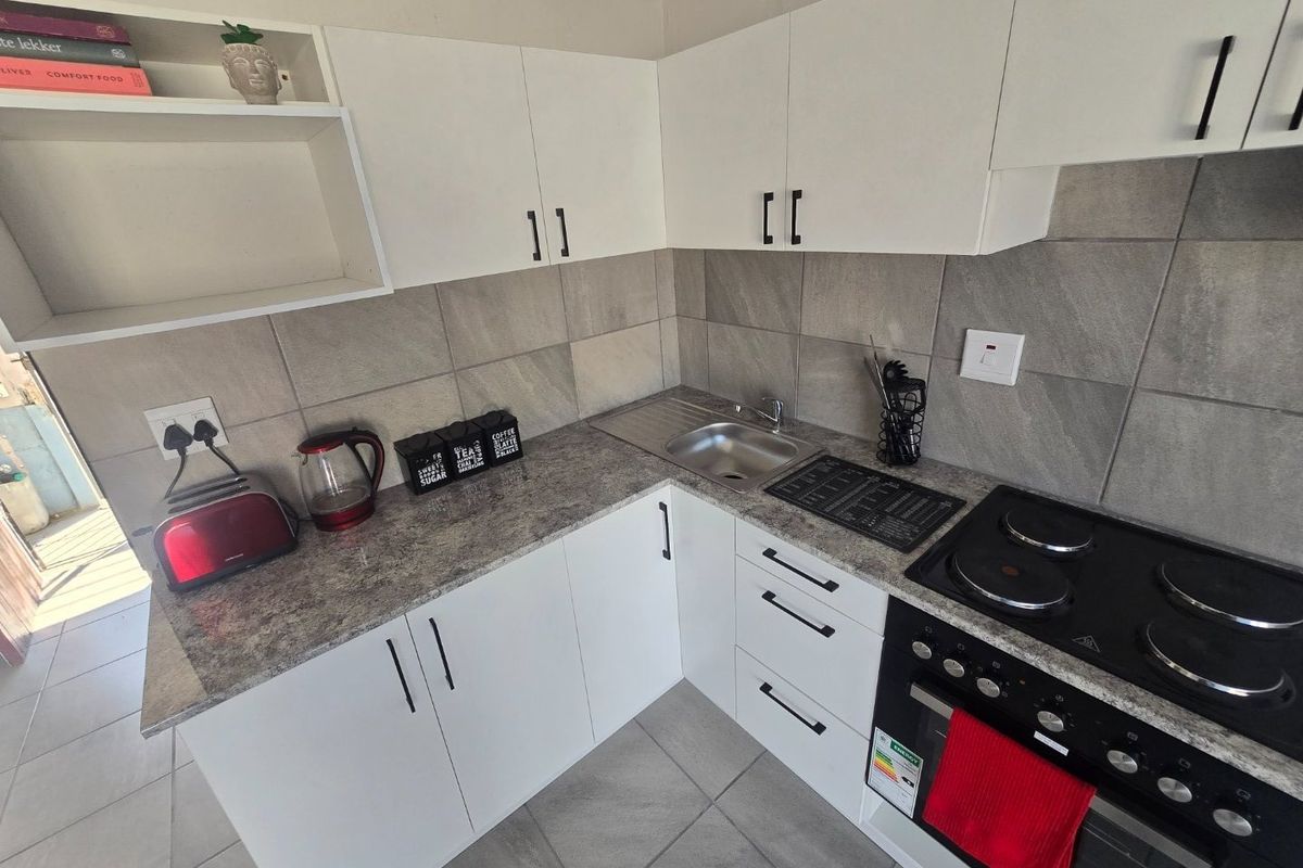 A compact, modern kitchen featuring white cabinetry, grey stone-look countertops, tiled backsplash, and integrated electric cooking appliances.