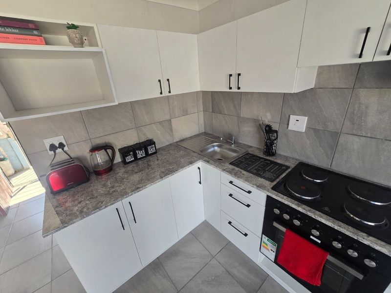 A compact, modern kitchen featuring white cabinetry, grey stone-look countertops, tiled backsplash, and integrated electric cooking appliances.