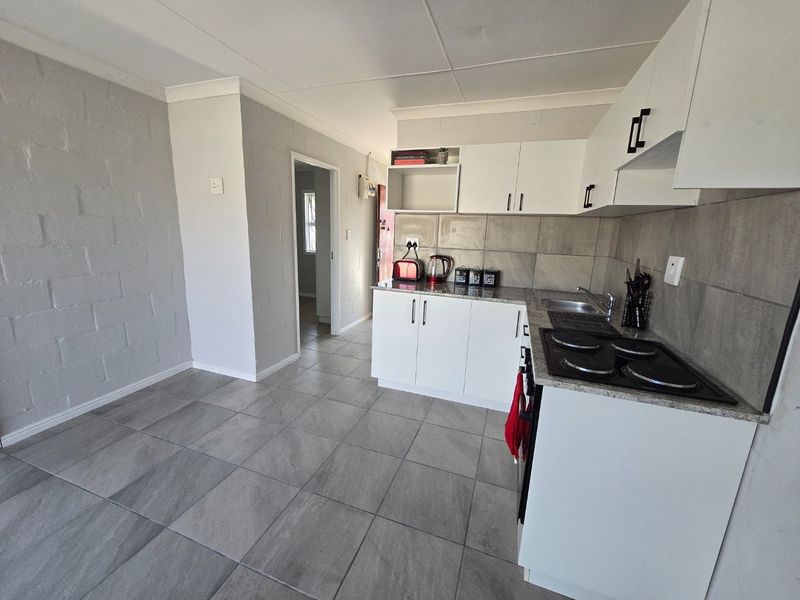 A functional kitchen featuring white cabinetry, stone-look countertops, an electric hob, and neutral tiled flooring, offering a clean and practical workspace.