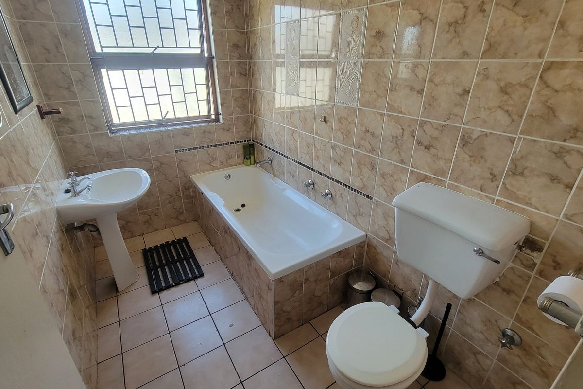 A functional bathroom featuring a pedestal basin, built-in bathtub, and toilet, finished with neutral ceramic wall and floor tiles.