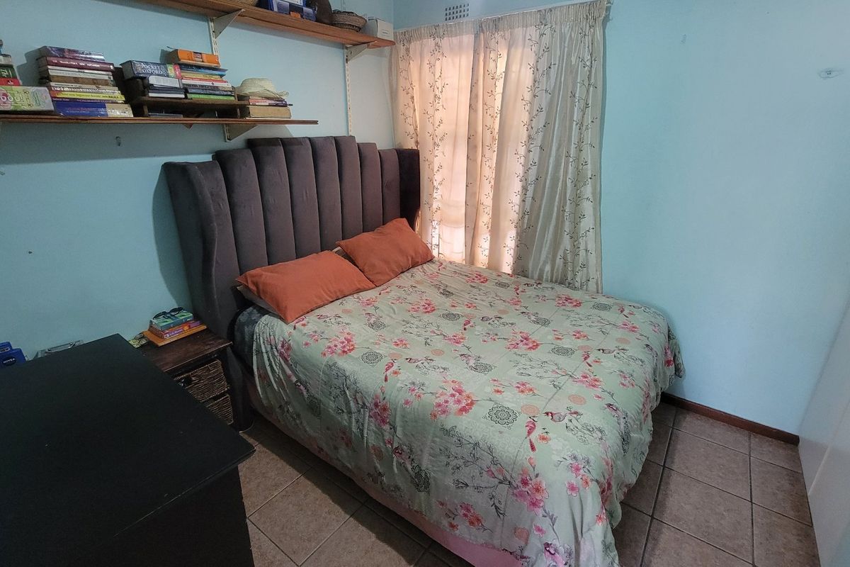 A functional bedroom featuring tiled flooring, built-in shelving, and a built-in wardrobe, offering a practical and comfortable living space.
