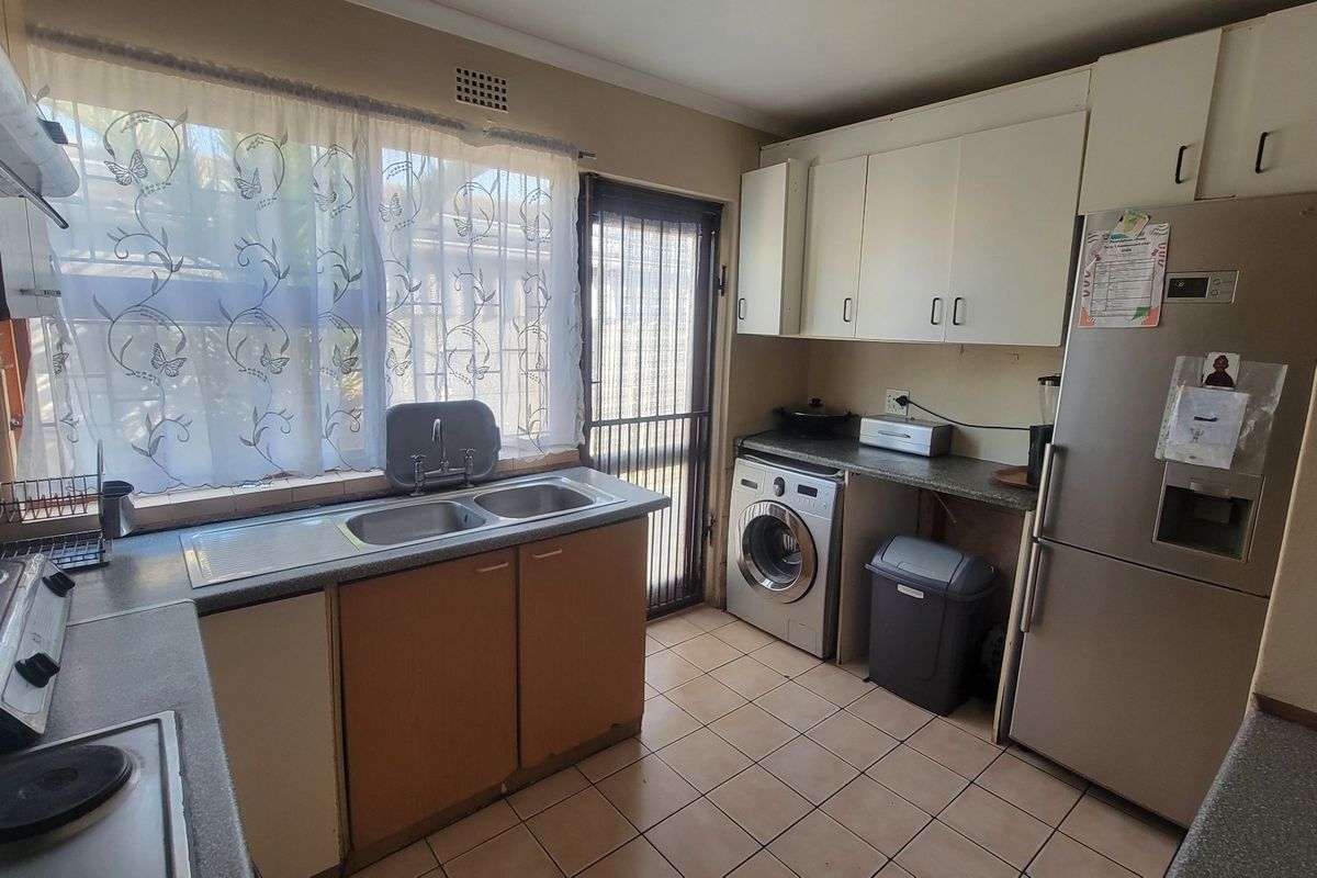 Functional kitchen featuring built-in cabinetry, double sink, tiled flooring, and direct access to the exterior via a security gate.
