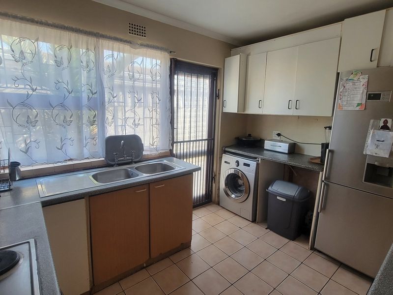 Functional kitchen featuring built-in cabinetry, double sink, tiled flooring, and direct access to the exterior via a security gate.
