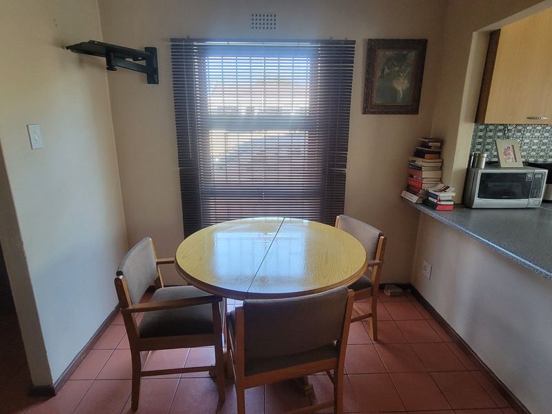Open plan dining area adjacent to a functional kitchen with tiled flooring, neutral walls, and built-in cabinetry.