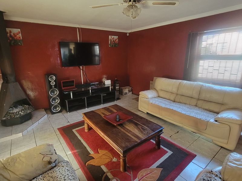 Living room featuring a freestanding fireplace, tiled flooring, and a ceiling fan, with red painted walls and a window with blinds.