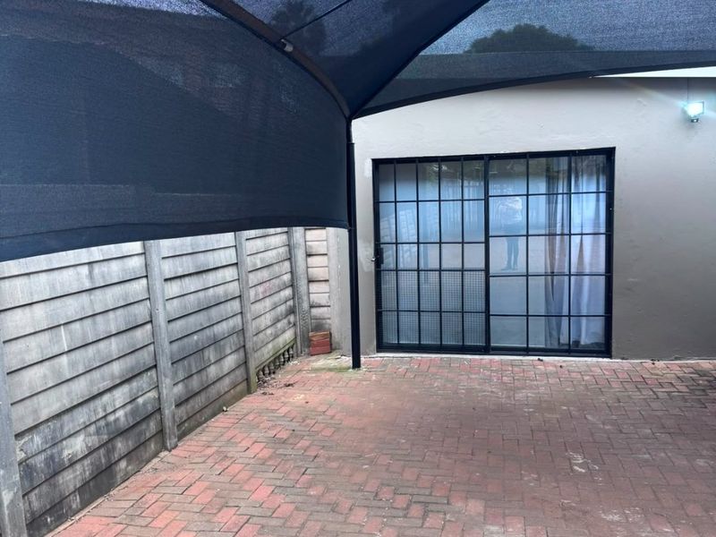 A private outdoor patio area featuring brick paving, a protective shade sail, and direct access to the interior via a sliding glass door.