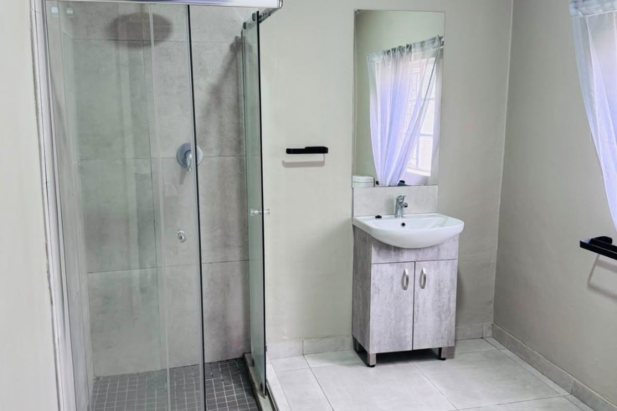 A clean, modern bathroom featuring a glass-enclosed shower, a vanity cabinet with a basin, and neutral floor tiling.