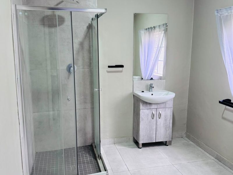 A clean, modern bathroom featuring a glass-enclosed shower, a vanity cabinet with a basin, and neutral floor tiling.