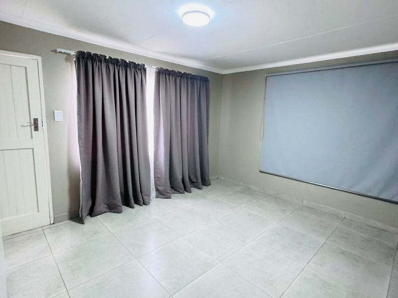 A clean, empty bedroom featuring neutral wall tones, tiled flooring, and a simple flush mount ceiling light fixture.
