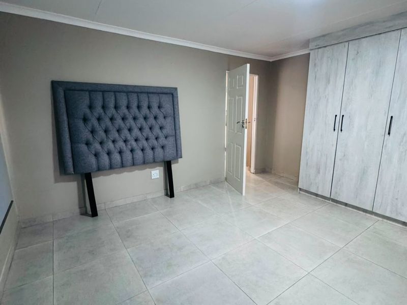 A clean, empty bedroom featuring neutral tiled flooring, built-in cupboards with light wood-grain finish, and a simple ceiling light fixture.