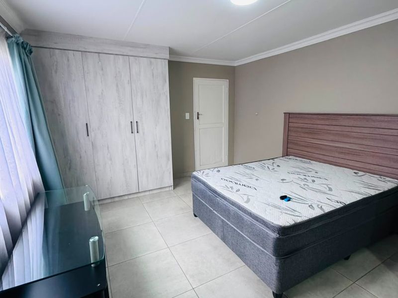 A well-maintained bedroom featuring neutral tiled flooring, built-in cupboards with a light wood finish, and a clean, simple layout.