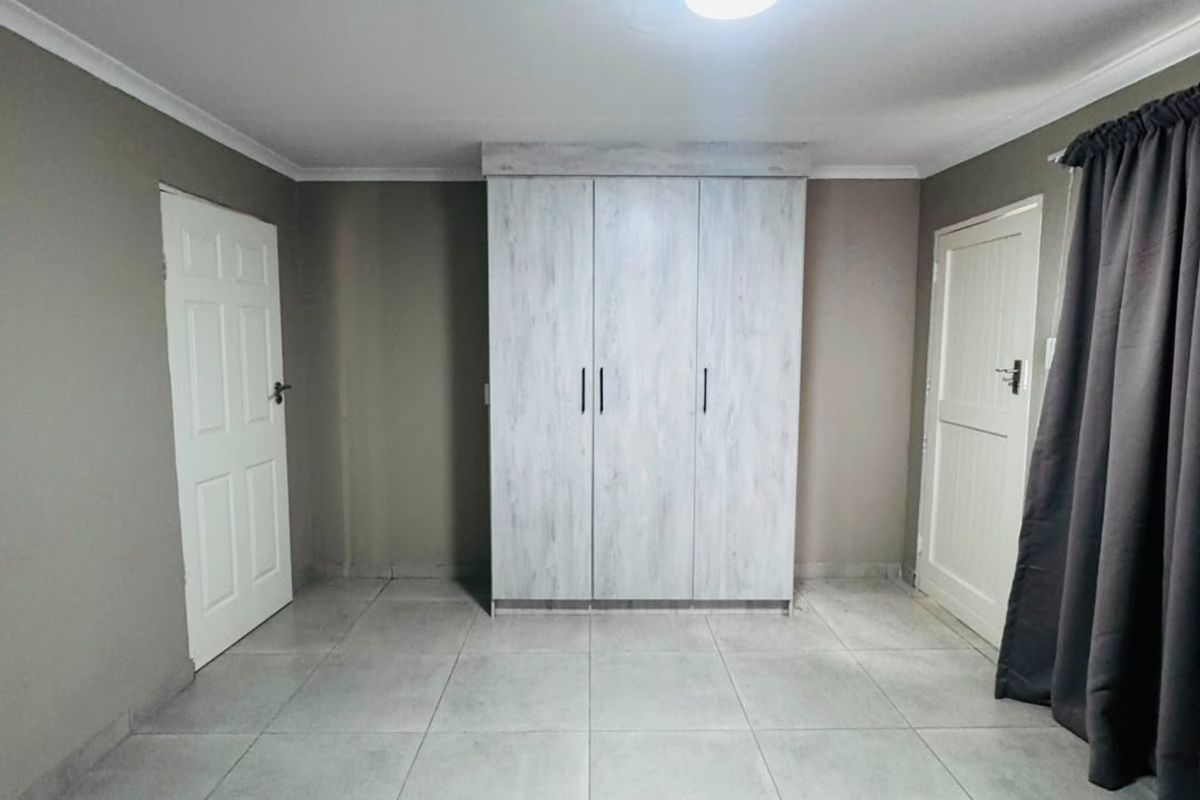 A clean, empty bedroom featuring neutral tiled flooring, a built-in wardrobe, and two access doors.