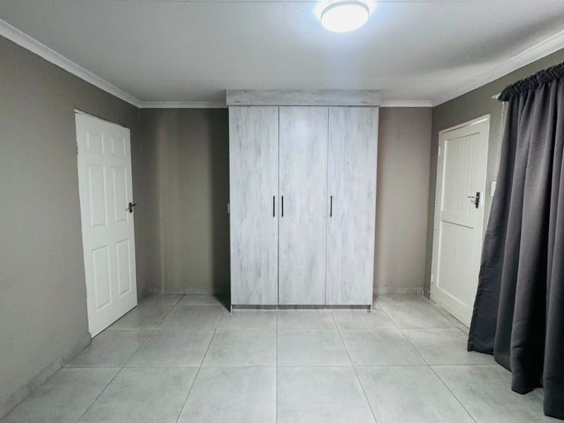 A clean, empty bedroom featuring neutral tiled flooring, a built-in wardrobe, and two access doors.