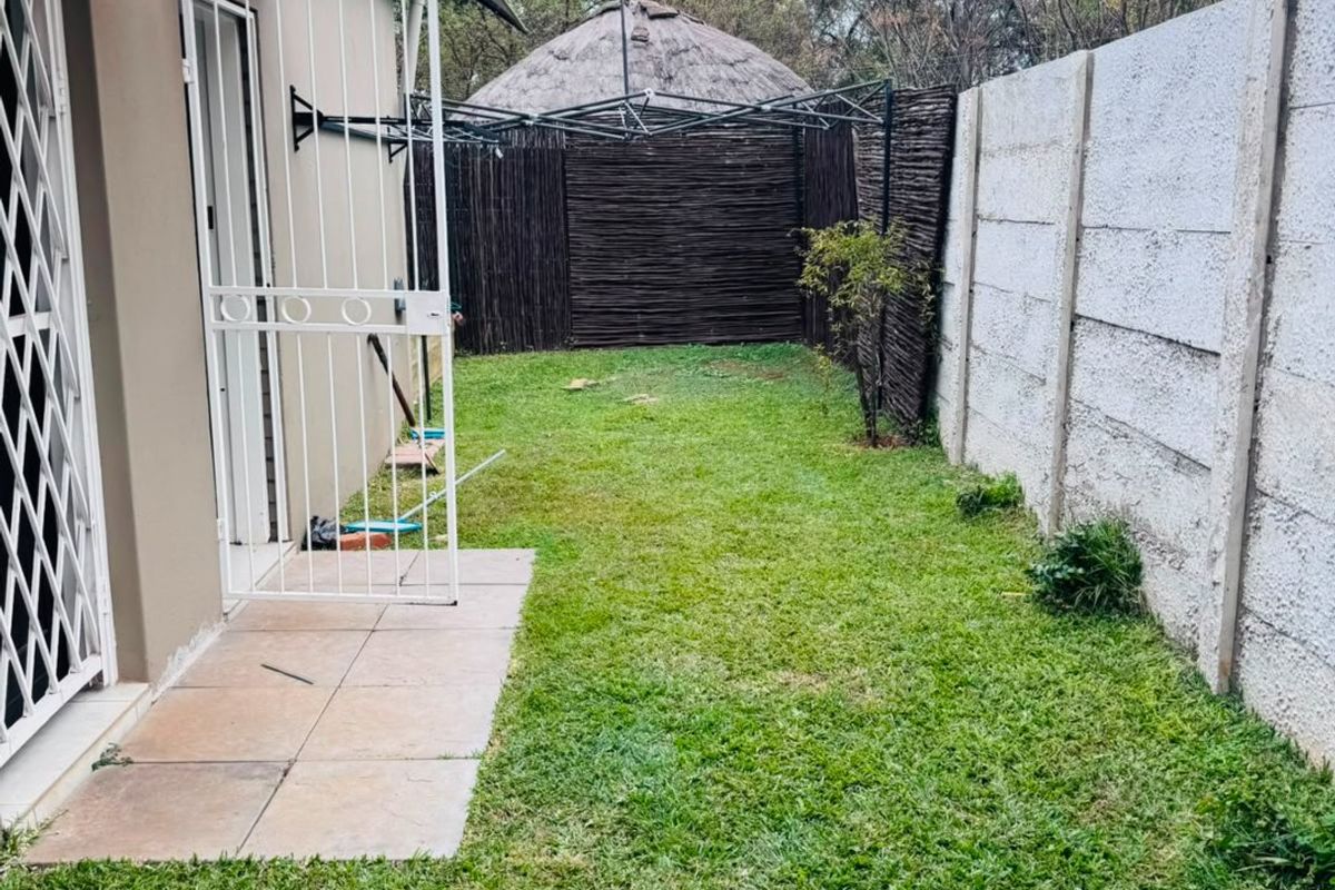 A private rear garden area featuring a small tiled patio, security gate, and precast concrete boundary wall.