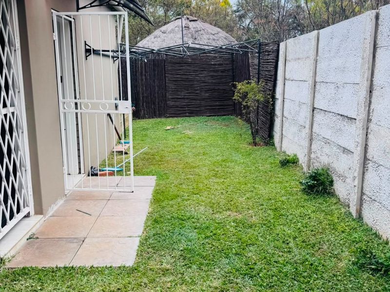 A private rear garden area featuring a small tiled patio, security gate, and precast concrete boundary wall.