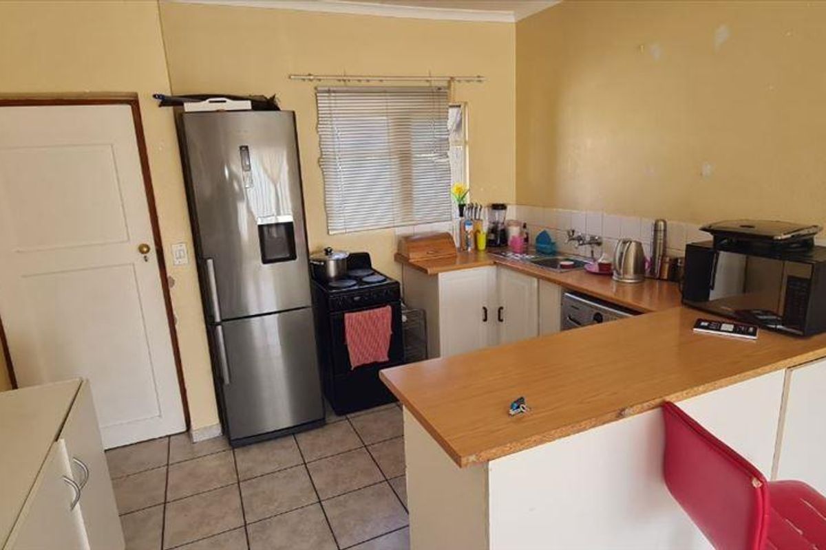 A functional kitchen featuring built-in cabinetry, laminate countertops, a breakfast bar, and tiled flooring, requiring cosmetic updates to improve its overall condition.