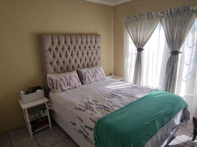 A standard bedroom featuring tiled flooring and large windows with curtain rails, providing natural light to the space.