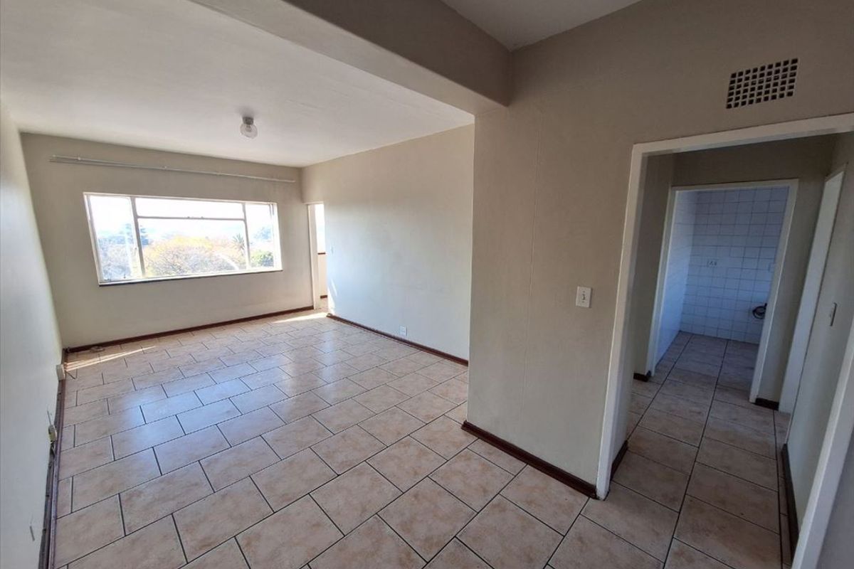 An empty, open-plan living area featuring neutral tiled flooring and natural light, with an adjacent tiled space visible through the doorway.