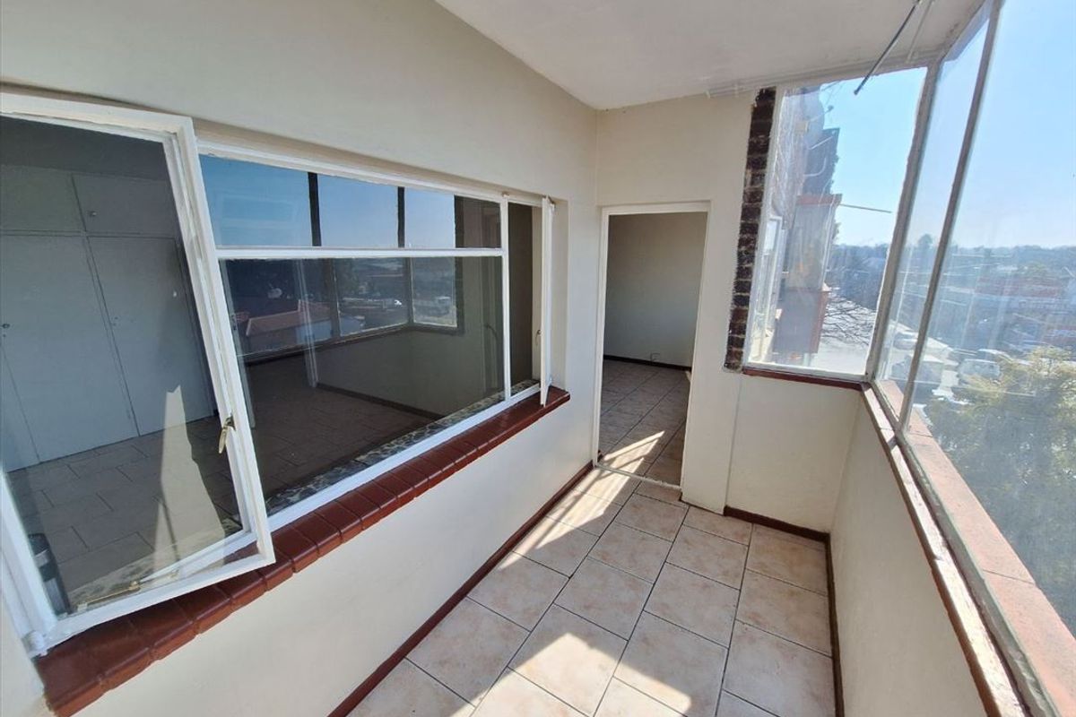 An enclosed balcony area featuring tiled flooring and large windows, offering an open space suitable for a sunroom or additional seating area.