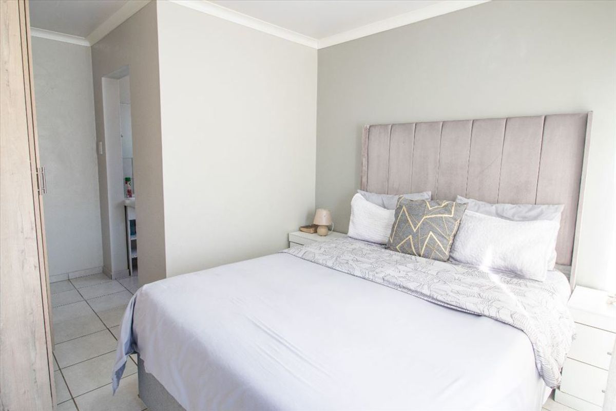 A well-maintained bedroom featuring neutral wall tones, tiled flooring, and a built-in wardrobe with access to an adjoining space.