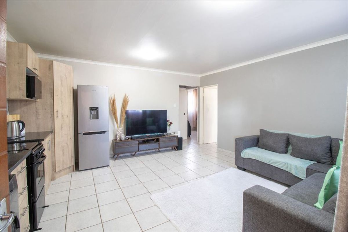 Open-plan living area featuring tiled flooring, neutral walls, and a compact kitchen with built-in cabinetry and black granite countertops.