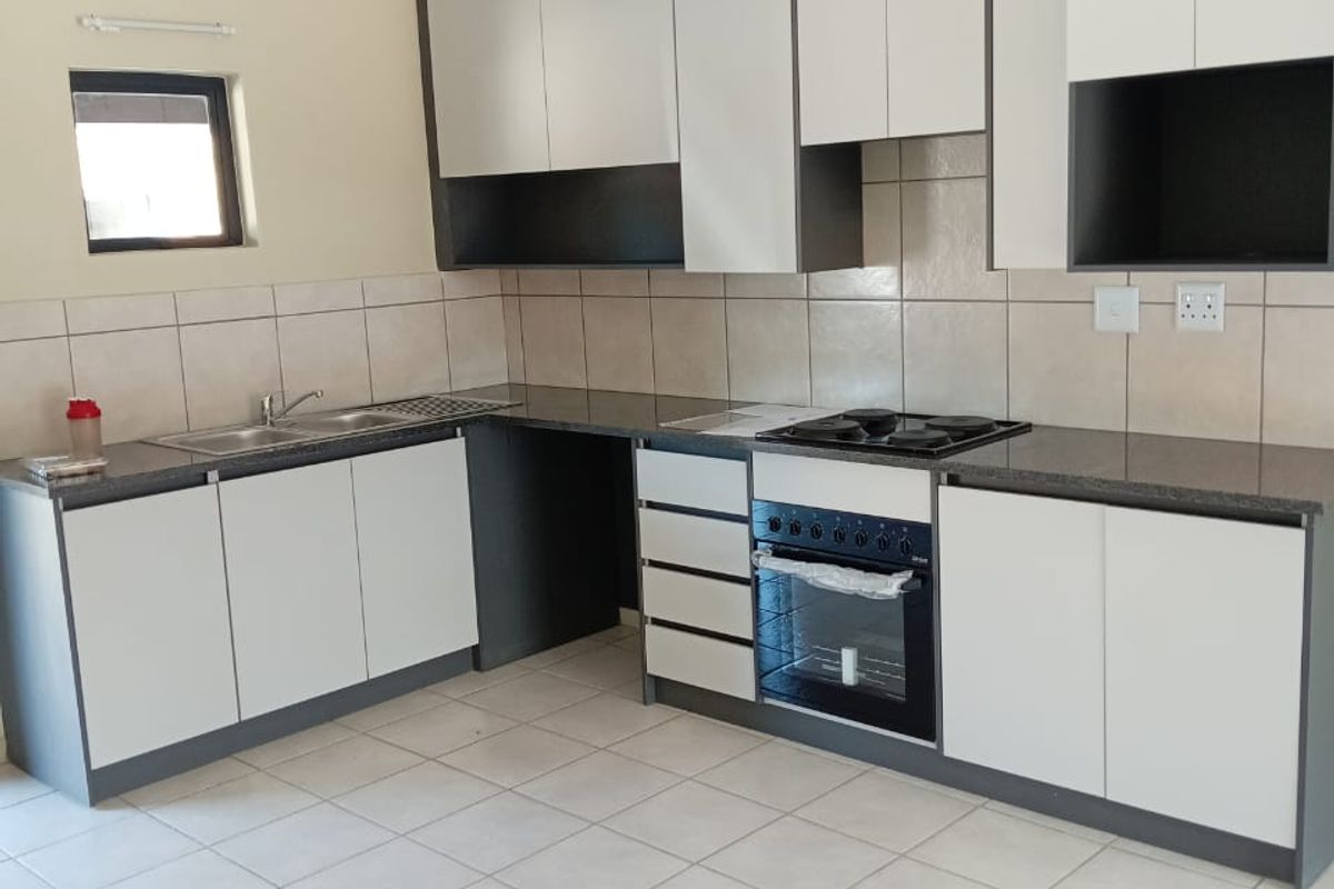 A clean, modern kitchen featuring two-tone cabinetry, granite countertops, a built-in oven and hob, and neutral tiled flooring.