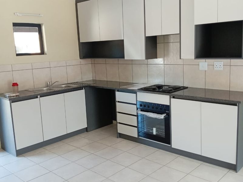 A clean, modern kitchen featuring two-tone cabinetry, granite countertops, a built-in oven and hob, and neutral tiled flooring.