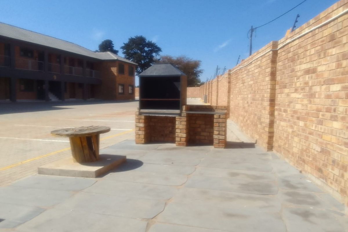 Outdoor communal area featuring a built-in brick braai, paved patio space, and secure perimeter walling with electric fencing.