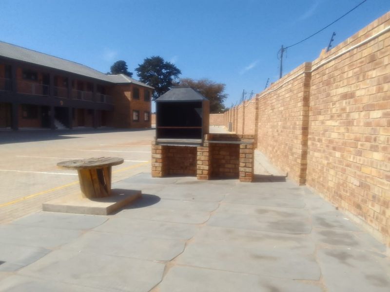 Outdoor communal area featuring a built-in brick braai, paved patio space, and secure perimeter walling with electric fencing.