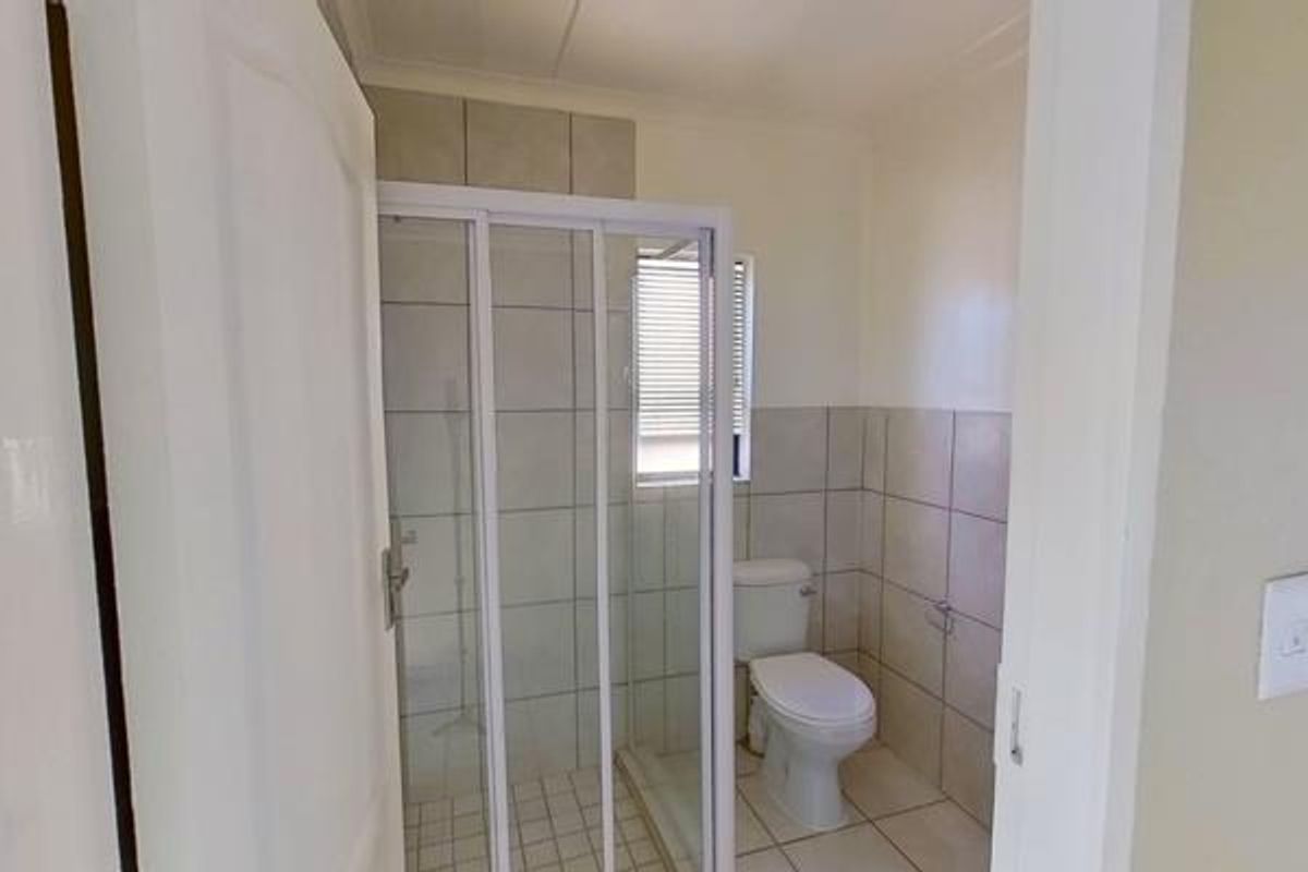 A functional bathroom featuring a shower enclosure, toilet, and neutral wall and floor tiling.