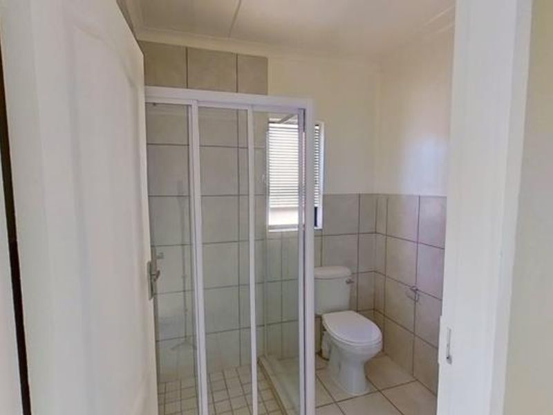 A functional bathroom featuring a shower enclosure, toilet, and neutral wall and floor tiling.