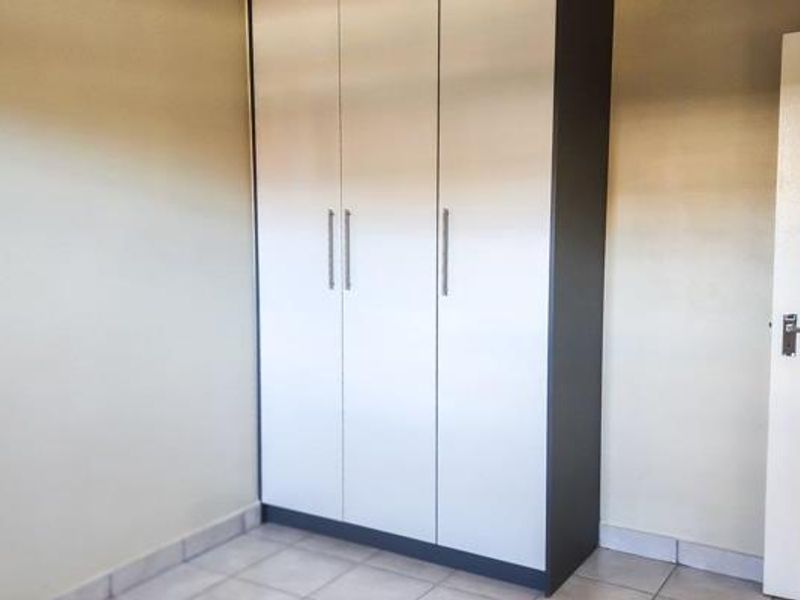 A clean, empty bedroom featuring neutral tiled flooring and a modern, full-height built-in wardrobe with sleek handles.