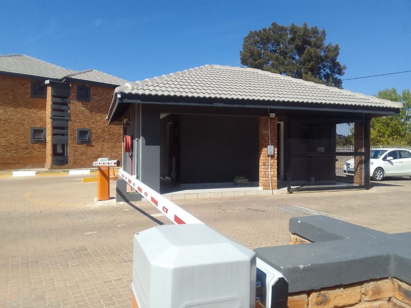 The property features a secure entrance with a boom gate, paved driveway, and brick-faced building structures under a tiled roof.