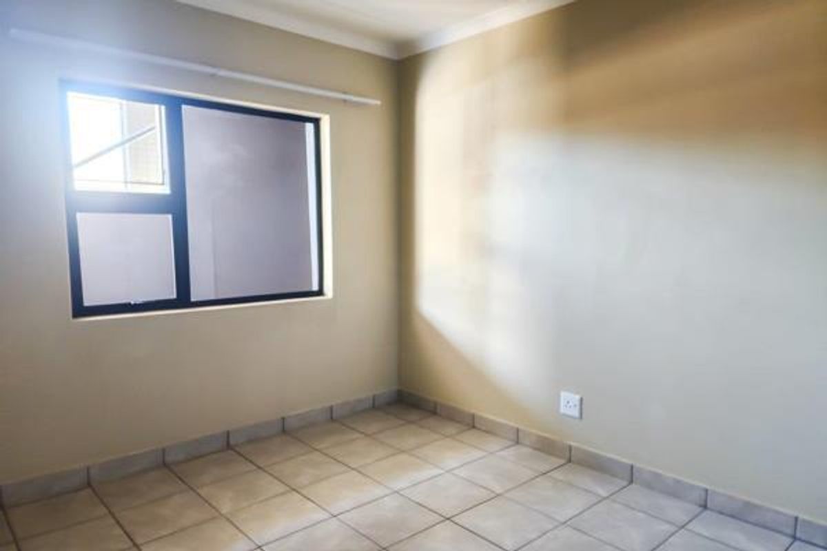 A clean, empty bedroom featuring neutral wall paint, tiled flooring, and an aluminium-framed window, providing a blank canvas for personalization.