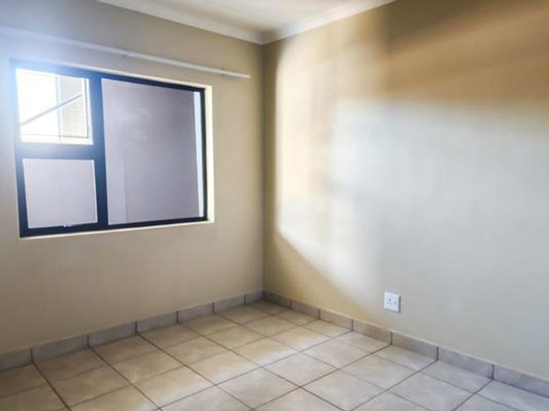 A clean, empty bedroom featuring neutral wall paint, tiled flooring, and an aluminium-framed window, providing a blank canvas for personalization.