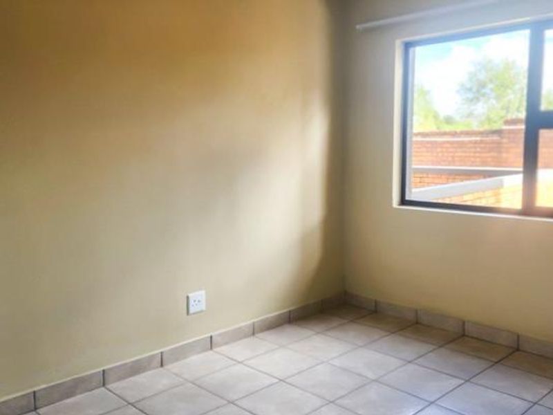 An empty bedroom featuring neutral wall paint, tiled flooring, and a large window providing natural light.