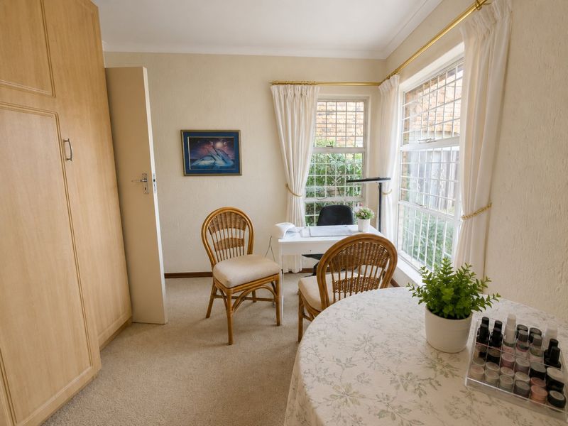 A bedroom featuring built-in wardrobes, carpeted flooring, and large windows with security bars, currently utilized as a home office or salon space.