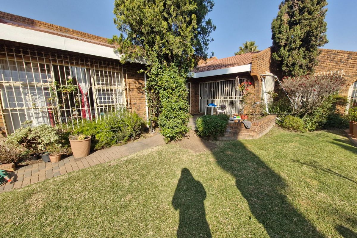 A rear view of the property featuring a brick facade, security bars on windows, a paved walkway, and a well-maintained garden lawn.