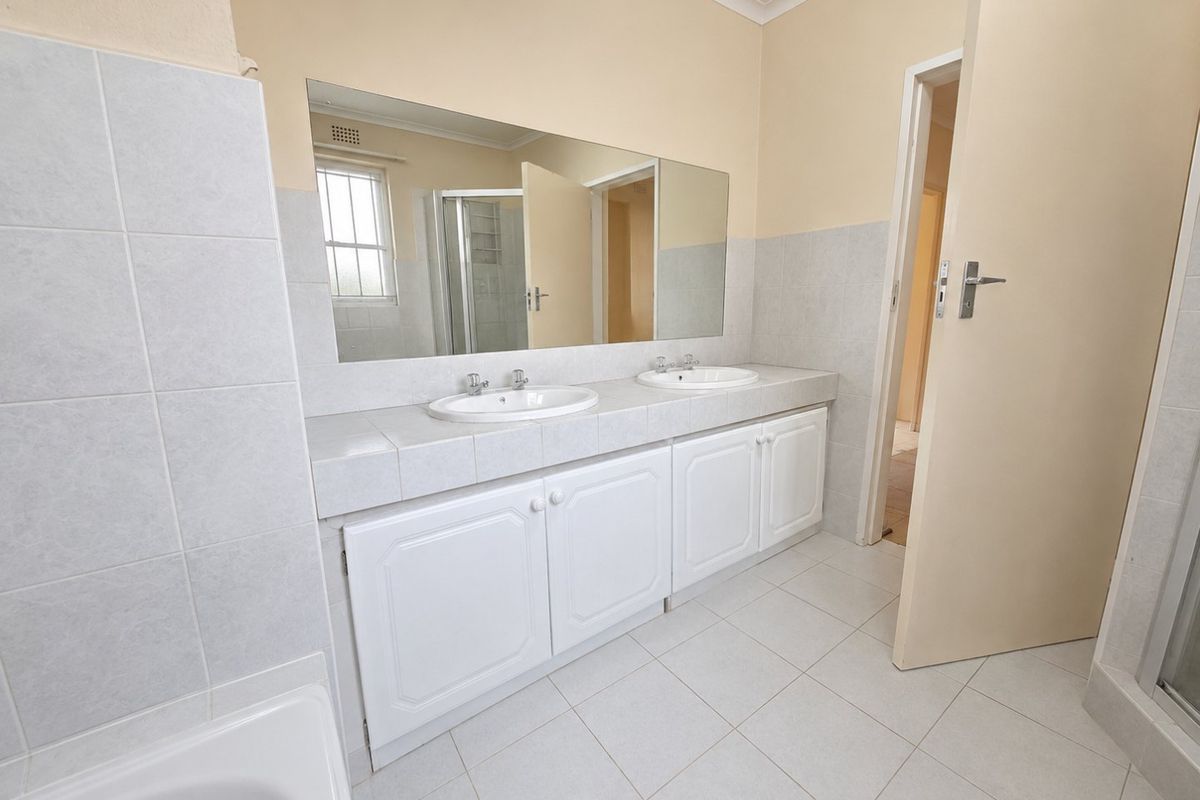 A clean and functional bathroom featuring a double vanity with white cabinetry, large wall mirror, and neutral floor tiling.